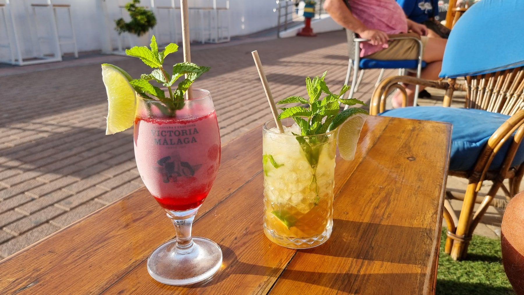 Zwei Drinks mit Minze und Limetten auf einem sonnigen Terrassentisch.