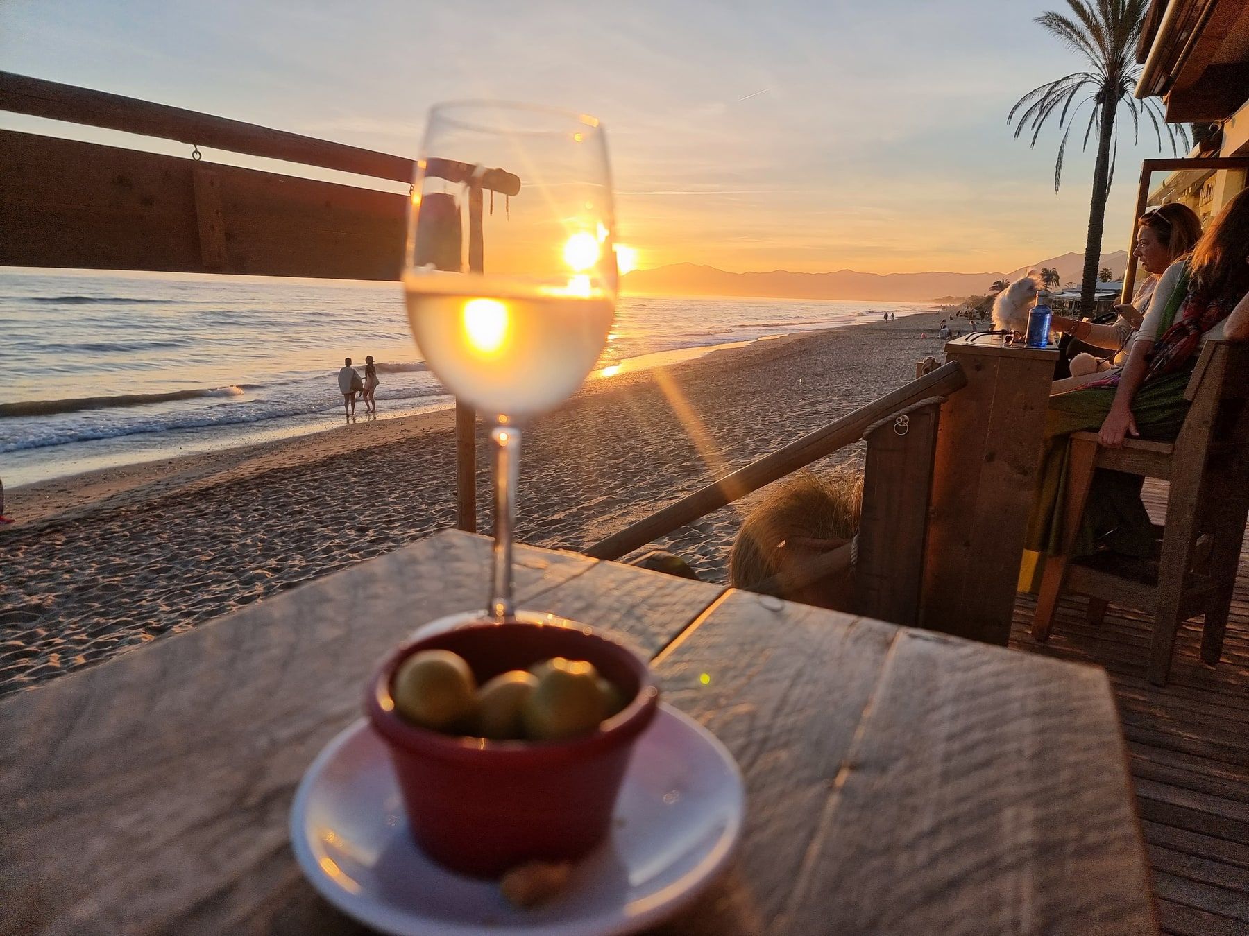 Ein Glas auf einer Strandterrasse vor dem Sonnenuntergang über der Bucht.